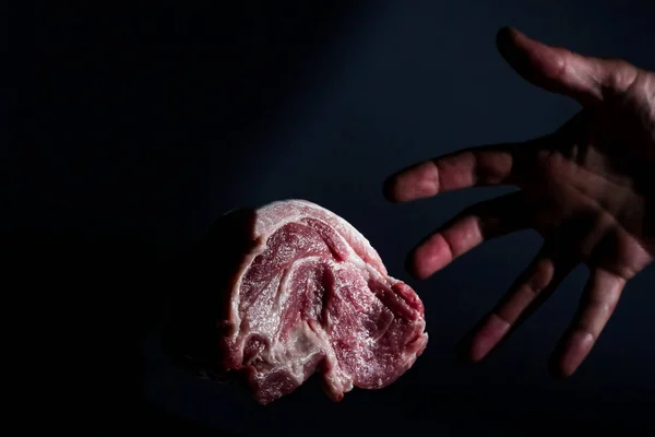 Рука людини і шматок м'яса рудої свинини на темному фоні — стокове фото
