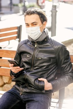 Koruyucu maskeli bir adam kameraya bakıyor ve şehir caddesinde cep telefonu kullanıyor. Dünya Covid-19 salgını sırasındaki sorumlu davranış. Virüs koruma kavramı