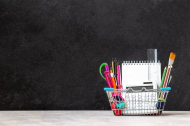 Siyah arka planda küçük bir alışveriş sepetinde parlak okul malzemeleri. Okul konseptine dönelim..