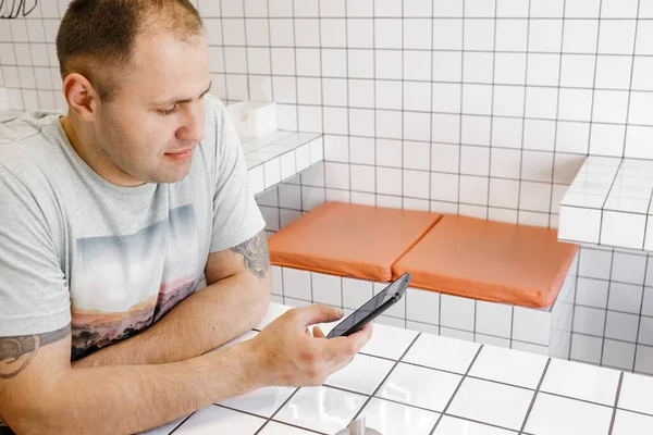 Concentrated handsome man freelancer use smartphone for work at table in cafe. Communication and technology concept. Side view.