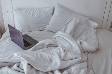 Laptoplu, dağınık, beyaz bir yatak. Yaşam tarzı yatak konseptine dayanır. Rahat çalışma alanı evden, ev eğlencesi ve rahatlama anı, rahatlama soyut kavram