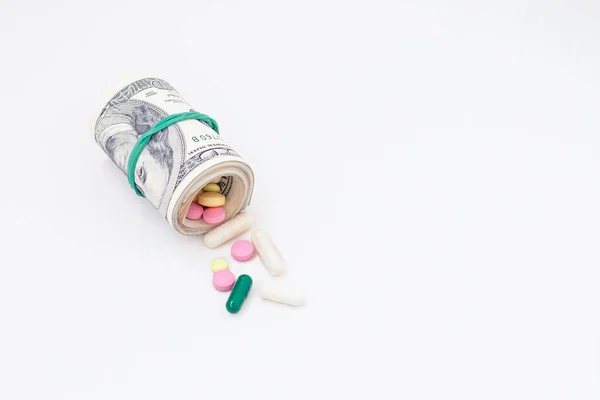 Prescription pills spilling out of roll of American money on white background. Medicine. World conspiracy, medical experiment, the secret government, coronavirus. prescription pills spilling out of roll of American money.