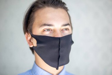 Siyah cerrahi maske takan yakışıklı bir gencin portresi. Stüdyoda çekilmiş, arka planda izole edilmiş. Covid19, sağlık ve tıp konsepti.