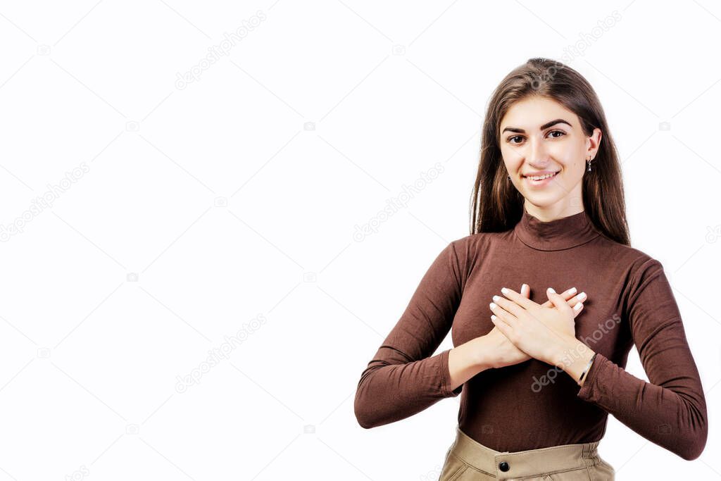Grateful young woman showing her heartfelt gratitude and thanks clasping her hands to her heart with a pleased smile on white background. Beautiful girl feeling love, gratitude, appreciation, thanking fate.