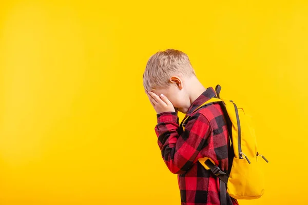 Crying child covering his eyes with fear, shame or resentment on yellow background. Concept of abuse, outsider in the children team, bullying.