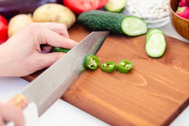 Çili biberi, salatalık, patates, fasulye pişirme sürecinde eller arka planda açık bir zemin üzerinde kesim tahtasının üzerinde. Mutfak konseptinde akşam yemeği hazırlamak yemek, aşçılık, sağlıklı yaşam tarzı