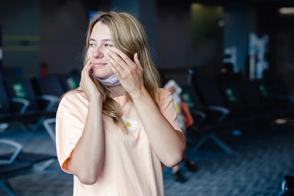 Girl wearing a protection mask for coronavirus or covid 19 rubbing her face with dirty hands in airport. Don\'t touch your face. Copy space.