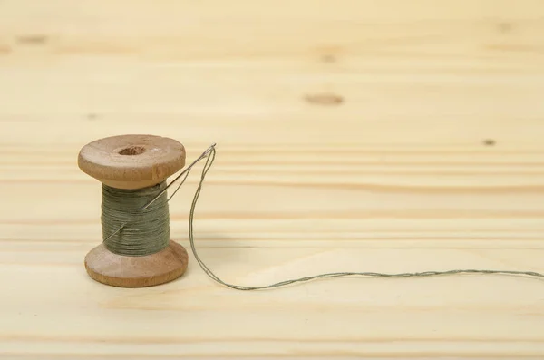 The old spool of thread with a needle on a wooden table.