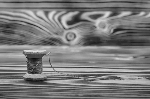 The old reel of thread and a needle on a wooden table in black and white.