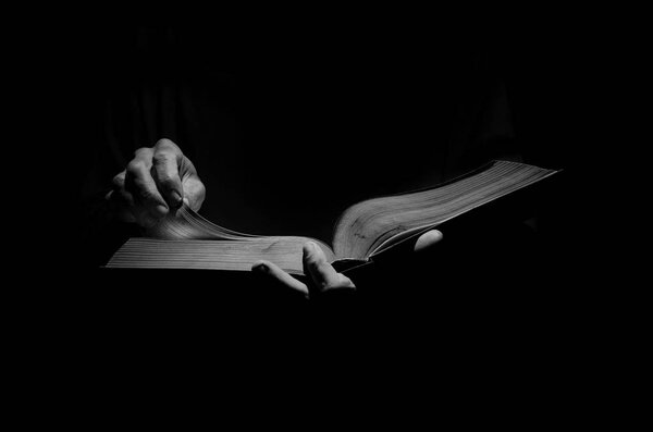 A man is reading a big book in black and white.