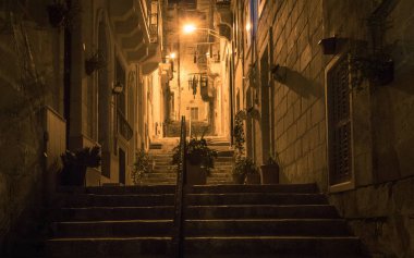 Gece görünümü üzerinde bir alleyway üst katta, ışıklar ve eski ev karşıtları tarafından örtülü Küpeşte gider. Çiçek pota. Elbise arka planda sarkıyordu. Malta'da bulunan.