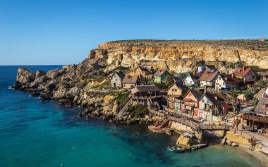Güzel manzara ev temel üzerinde. Bir çizgi roman tarzı çok sayıda renkli ev ile köy. Malta çapa koyunda yer alan. Mavi gökyüzü, deniz ve kayalıklarla ön planda. Konteyner gemileri arka planda