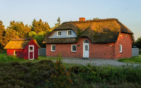 Panoramik bir geleneksel tuğla inşa ev, thatched çatı ve ön planda birçok yeşil küçük yazlık. Güzel bir manzara tatil evde yakınındaki Kuzey Deniz günbatımı sırasında.
