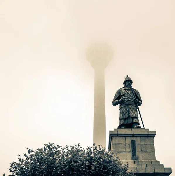 Busan Tower and Statue of Admiral Yi Sun-sin in front on a foggy day. Jung-gu, Busan, South Korea. Asia.