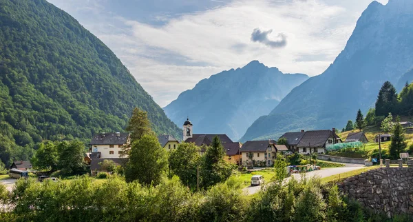 Panorama con edificios, carretera principal e iglesia parroquial dentro del paisaje de montaña de la aldea Log pod Mangartom. Bovec, Eslovenia, Europa . — Foto de Stock