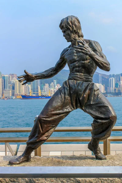 Bruce Lee Heykeli gezinti güvertesinin yanındaki Yıldız Bulvarı 'nda. Arka planda Hong Kong Adası 'nın silüeti var. Tsim Sha Tsui, Hong Kong, Çin.