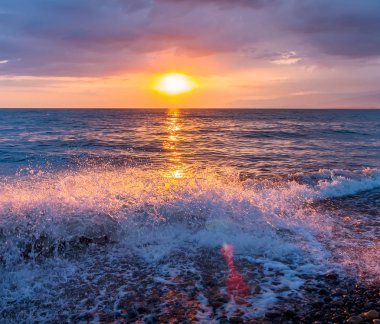 Denizin dalgaları ve çakıl sahil manzaralı üzerinde parlak günbatımı
