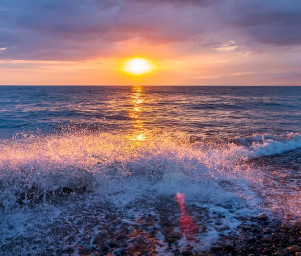 Denizin dalgaları ve çakıl sahil manzaralı üzerinde parlak günbatımı