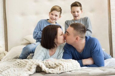 Aile anne, baba ve iki çocuk bir yatakta yatıyordu. Birbirleriyle ve üzerlerinde gülmeye çocuk öpüşme anne. Gülümseyen ve aile sarılma. Kaç anne gülümseyerek onların oğulları öpüşme.