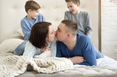 Aile anne, baba ve iki çocuk bir yatakta yatıyordu. Birbirleriyle ve üzerlerinde gülmeye çocuk öpüşme anne. Gülümseyen ve aile sarılma. Kaç anne gülümseyerek onların oğulları öpüşme.