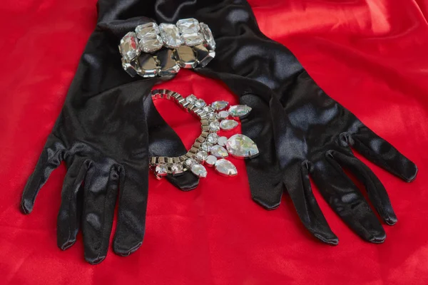 Deux jolis gants noirs à côté de collier brillant et bracelet sur fond rouge — Photo
