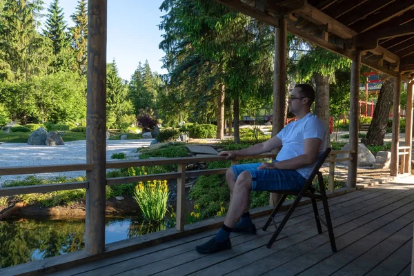 Un joven se sienta en una silla plegable en un porche de madera al amanecer y mira hacia el futuro — Foto de Stock