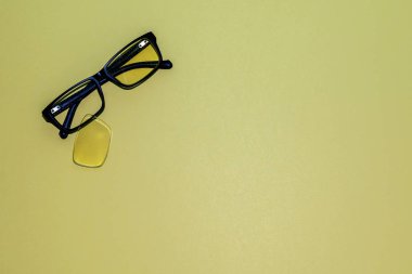Katlanmış kollar ve çerçeveden düşen bir lens ile kırık gözlük sarı bir yüzey üzerinde yalan. Yukarıdan görüntüle