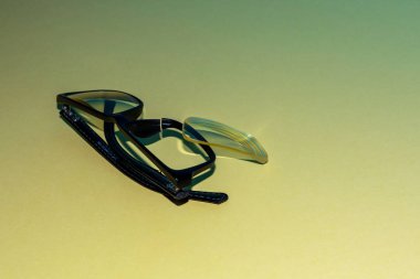 Katlanmış kemerli gözlükler sarı bir yüzey üzerinde direner. Yukarıda kırık bir çerçeve düştü bir lens yatıyor