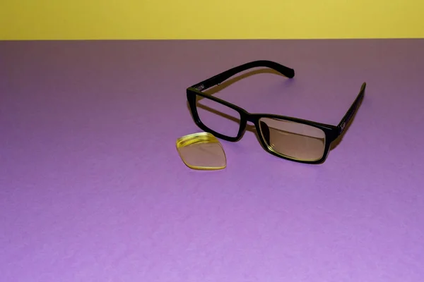 Zerbrochene Gläser liegen auf einer violetten Oberfläche. In der Nähe liegt eine gelbe Linse, die aus dem Rahmen gefallen ist. gelber Hintergrund zurück — Stockfoto