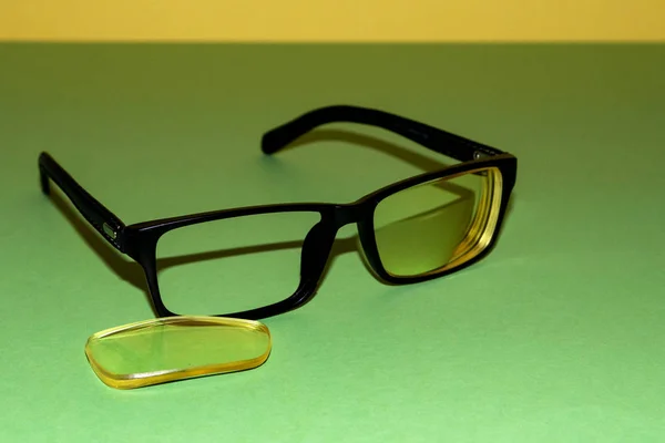 Złamane okulary leżą na zielonej powierzchni. W pobliżu znajduje się żółty obiektyw, który spadł z ramy. Żółte tło wstecz — Zdjęcie stockowe