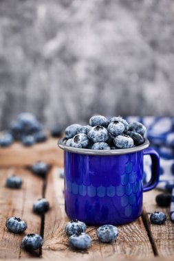 Olgun taze yaban mersini ve rustik zemin üzerine mavi Mine kupa