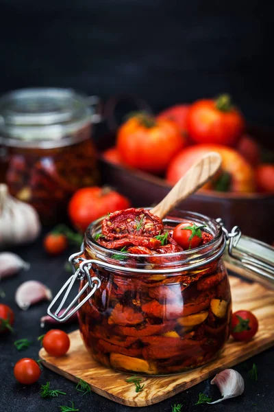 Kurutulmuş domates sarımsak ve koyu arka plan üzerinde bir kavanoza zeytin yağı ile