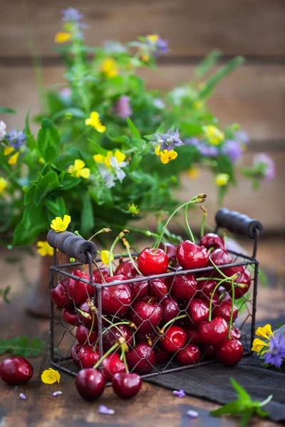 Tahta arka planda metal sepetin içinde taze kirazlar.