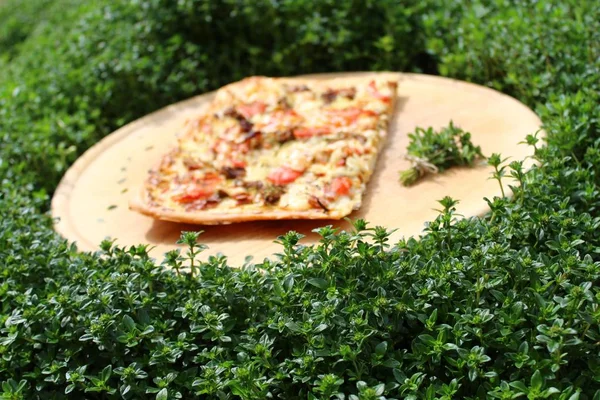 a piece of pizza on a wooden board in a thyme field