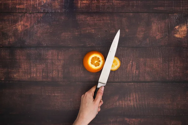 Knife cut the orange on the wooden table