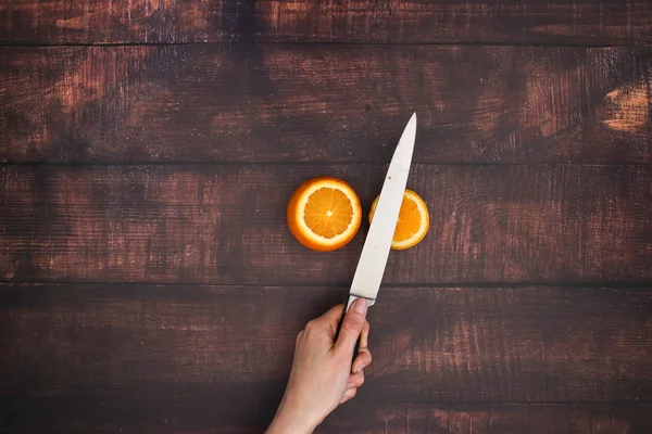 Knife cut the orange on the wooden table