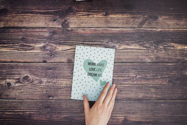 Woman's hand and blue motivation notebook on wooden table