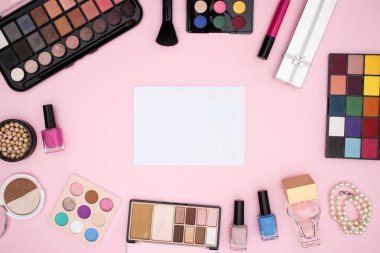 Pembe arka planda beyaz kağıt etrafında ürünler makyaj 
