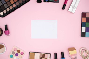 Pembe arka planda beyaz kağıt etrafında ürünler makyaj 