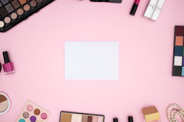 Pembe arka planda beyaz kağıt etrafında ürünler makyaj 