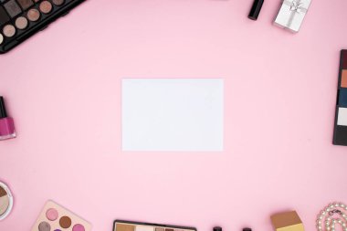 Pembe arka planda beyaz kağıt etrafında ürünler makyaj 