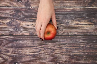 Kadının eli masanın içinden bir tane kırmızı ve taze elma alır. 