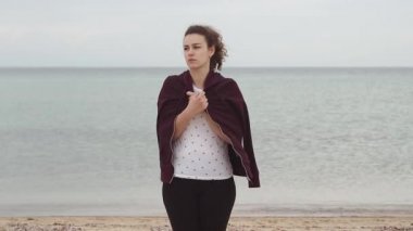 Rüzgar eserken sahilde duran genç kadın. Genç kadın soğuk havalarda sweatshirt ile kendini elbise