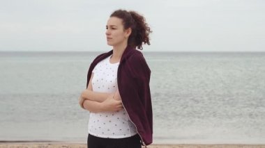 Rüzgar eserken sahilde duran genç kadın. Genç kadın soğuk havalarda sweatshirt ile kendini elbise