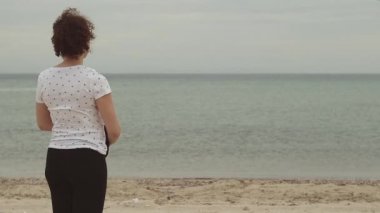 Rüzgar eserken sahilde duran genç kadın. Genç kadın soğuk havalarda sweatshirt ile kendini elbise