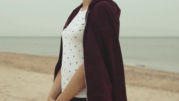 年轻女子站在沙滩上 风在吹 年轻女子在寒冷的天气穿着运动衫 — 图库视频影像