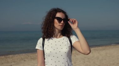 Güzel genç kadın portresi güneş gözlüğü almak ve güneşli bir günde sahilde etrafında izlerken