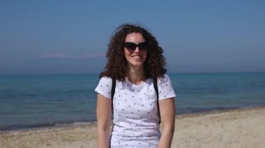 Güneşli bir günde sahilde gülümseyen kıvırcık saçlı güzel genç kadın portresi