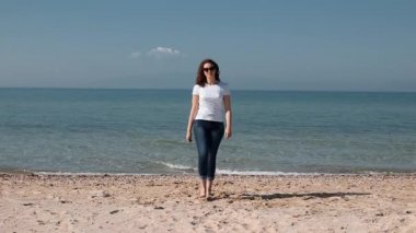 Güneşli bir günde sahilde yürüyen ve yakına gelen güzel genç kadın