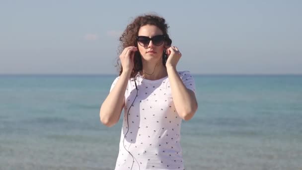 年轻漂亮的女人把耳机在沙滩上听音乐 — 图库视频影像